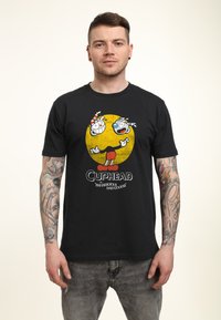 Schwarzes T-Shirt mit einem bunten Cuphead-Graphic und einem gelben Kreis-Hintergrund. Das Material wirkt weich; das Design umfasst Cartoon-Charaktere und Text.