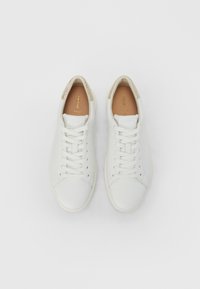 Άσπρα δερμάτινα αθλητικά παπούτσια με επίπεδες κορδόνια και υφασματικό χρυσό διακοσμητικό στη φτέρνα. Λείο επάνω μέρος και μινιμαλιστικός σχεδιασμός.