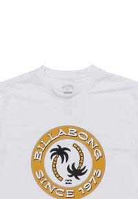 Biała koszulka z krótkim rękawem z okrągłym wzorem przedstawiającym palmy oraz napisem "BILLABONG SINCE 1973" w kolorze czarnym i złotym. Gładka faktura materiału.