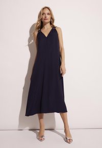 Granatowa sukienka bez rękawów z dekoltem w serek i złotymi akcentami na ramiączkach. Gładki, lejący materiał, sięgająca kostek w luźnym fasonie.