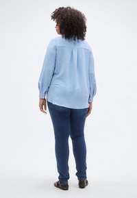 Ανοιχτό μπλε πουκάμισο με μακριά μανίκια, υφαντό σχέδιο, μανσέτες με κουμπιά και πιέτα στην πλάτη, συνδυασμένο με στενά σκούρα μπλε τζιν και καφέ παπούτσια.