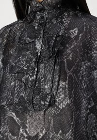 Blusa con stampa a serpente nera e grigia, caratterizzata da un alto colletto arruffato, chiusura a bottoni frontale e tessuto testurizzato con un leggero lucido.