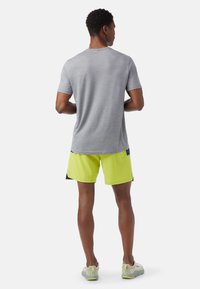 Grå kortärmad skjorta i kombination med ljusgula shorts, med en bekväm passform och slät textur. Outfitten har kontrasterande marinblå detaljer.