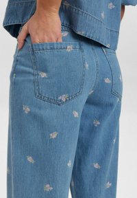 Lichtblauwe denim jeans met bloemenpatroon accenten. Heeft een achterzak, recht model en zichtbare stiksels langs de naden.