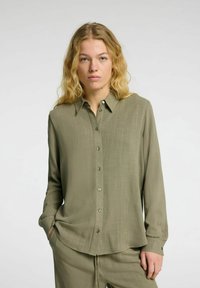 Olijfgroene, langemouwen blouse met knopen in een gladde, lichtgewicht stof, met een puntige kraag en subtiele textuur, gecombineerd met bijpassende broek.