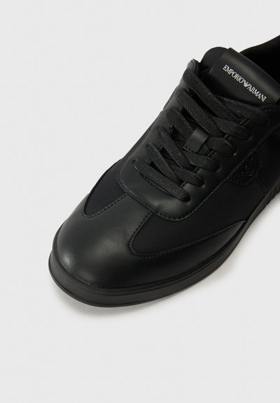 Black sneaker featuring a mixture of smooth leather and textile materials, rounded toe, flat sole, and lace-up closure with logo detail.