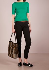 Grön figurnära topp, svarta slim-fit byxor, svarta lackloafers, brun bälte och en randig vävd handväska med svarta och guldfärgade accenter.