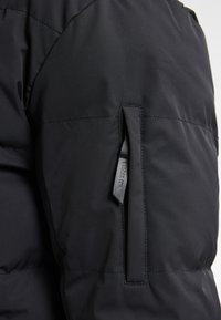 Giubbotto puffer nero con tessuto testurizzato, design isolato e tasca laterale con zipper dotata di una linguetta in pelle.