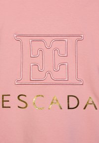 Tessuto di cotone rosa con un logo ricamato che presenta le lettere "E" e "H" contornate in bianco e la parola "ESCADA" in foglia d'oro sotto.