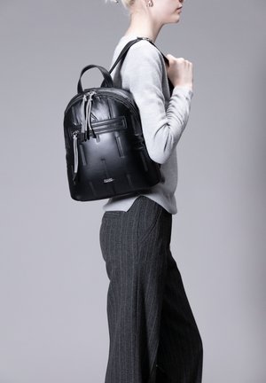 Schwarzer Leder-Rucksack mit strukturiertem Finish, Reißverschlusstasche und verstellbaren Riemen. Kompakte Form mit runder Basis und oberem Griff.
