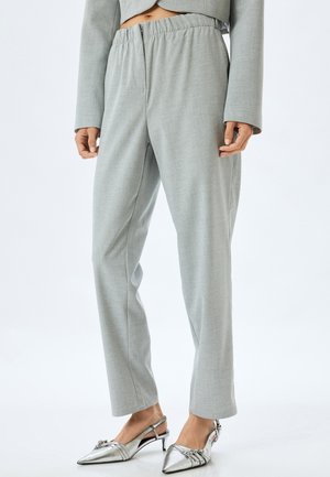 Lichtgrijze taps toelopende broek van een textuurstof, met een elastische tailleband en zijzakken, gecombineerd met zilveren spitse hakken.