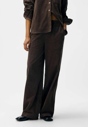 Ensemble en velours côtelé marron comprenant une chemise à boutons et un pantalon large, caractérisé par des nervures verticales et une coupe décontractée.