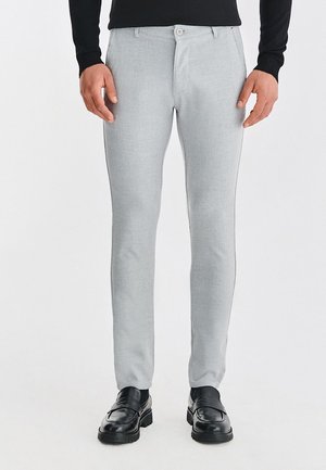 Jasnoszare, dopasowane spodnie o gładkiej fakturze, z zapięciem na guzik i szlufkami na pasek. W połączeniu z czarnymi butami.