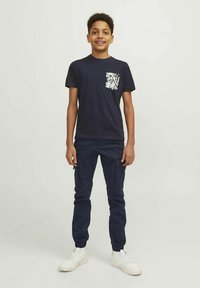 Μπλε ναυτικό μπλουζάκι με λευκό τυπωμένο λουλουδάτο σχέδιο στην τσέπη, συνδυασμένο με μπλε ναυτικό παντελόνι με τσέπες cargo και λευκά αθλητικά παπούτσια.