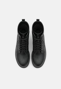 Botas de tobillo de cuero negro con un acabado texturizado, punta redonda y diseño de cordones. Incluyen una pestaña en la parte trasera y suela blanca en contraste.