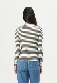 Long-sleeve top in olive green and white stripes, made of ribbed fabric. Paired with high-waisted blue denim jeans. Back view.