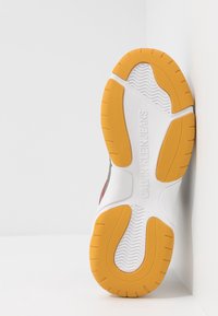 Semelle de sneaker blanche avec des accents orange, dotée de motifs de grip texturés et d'un logo surélevé "CALVIN KLEIN JEANS". Design plat et ovale.