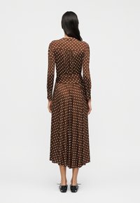 Μακρύ, καφέ, διαφανές φόρεμα με λευκές πουά. Διαθέτει μακριά μανίκια και πλισέ φούστα. Σχεδιασμένο με εφαρμοστό μπούστο και ζώνη στη μέση.