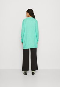 Pull mint vert à manches longues, coupe loose, avec un ourlet côtelé, associé à un pantalon noir large et des sandales à talons vertes.