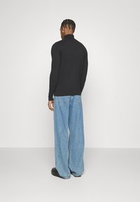 Maglione nero a coste con collo alto abbinato a jeans a gamba larga di un blu chiaro. L'outfit presenta una vestibilità comoda e una texture liscia, con dettagli minimi.