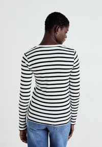 Haut à manches longues avec des rayures horizontales noires et blanches. Fabriqué dans un matériau doux, il présente un col rond et une coupe ajustée.