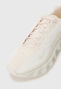 Jasno beżowe sportowe sneakersy z perforowanym czubkiem, fabryczną cholewką, sznurowaniem oraz teksturowaną podeszwą z subtelnym logo z boku.