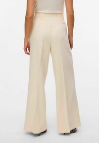 Pantalons larges crème avec taille haute, texture lisse et design épuré. Présente un pli subtil sur le devant pour une touche supplémentaire de détail.