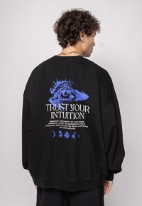 Black oversized sweatshirt featuring a large graphic print of an eye and text on the back in white and blue with moon phases at the bottom.