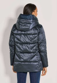 Donkerblauwe pufferjas met capuchon, voorzien van een gequilt ontwerp en elastische onderkant. Zacht, glanzend materiaal. Achteraanzicht weergegeven.