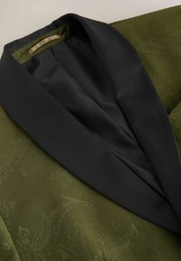 Tume oliivroheline sametbleiser, millel on peenus paisleimuster ja kontrastne sile must sateenist kaelus, esitatud lamades.