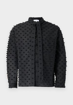 Svart skjorte med teksturert stoff, prydet med putete prikker, lange ermer, ståkrage, frontknapper og brystlomme.