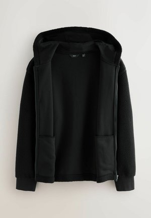 Sort hættejakke med et blødt, tekstureret ydre lag. Har to forlommer, en lynlåslukning og en kontrasterende glat inderside.