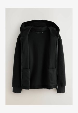 Zwarte hoodie met een zachte, textuurachtige buitenlaag. Beschikt over twee voorzakken, een ritssluiting en een contrasterende gladde binnenvoering.