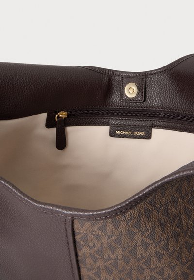 Gros plan sur un sac cabas Michael Kors marron ouvert, laissant voir sa doublure beige, sa poche intérieure zippée, son bouton-pression doré et son extérieur à motifs.