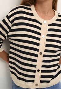 Gestreifter Cardigan in Creme und Marineblau, mit Rundhalsausschnitt, Knopfverschluss vorne und gerippten Bündchen und Saum. Weiche Stricktextur.