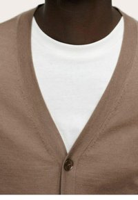 Cárdigan marrón con un profundo escote en V, cierre de botones y textura ligera. Llevado sobre una camiseta de cuello redondo blanca, mostrando un estilo con capas.