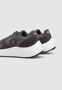 Baskets grises à dessus lisse, accents en daim, semelle intermédiaire blanche épaisse et semelle extérieure noire. Présentent un logo circulaire sur le côté.