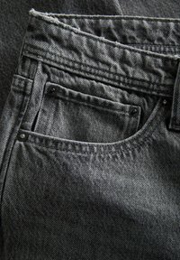 Mustade teksade lähivõte, kus on nähtav eesmine tasku, millel on naelad, õmblused ja tekstuuriga kangaste detailid.