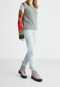Stickad tröja med grå kropp och färgglada, mönstrade ärmar. Parat med ljusblå jeans och beige snörstövlar med svarta sulor.