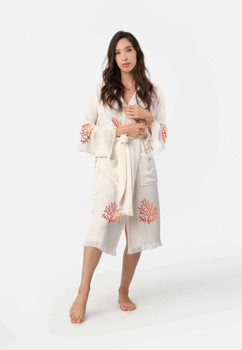 Biely bavlnený župan s koralovými vyšívanými detailmi, s viazaním v páse, zvonovými rukávmi a strapcovými zakončeniami. Obsahuje dve predné vrecká.