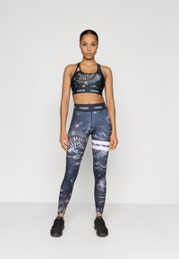 Conjunto desportivo composto por um sutiã e leggings azuis e estampadas, com designs gráficos e detalhes em preto sólido. O material parece elástico e ajustado.