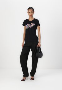 Black cotton T-shirt with colorful floral graphic, paired with black wide-leg pants and a small black handbag. Worn with black heeled sandals.