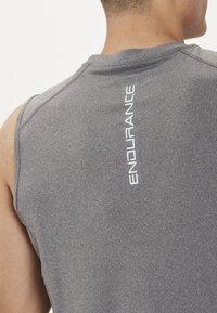 Ærmeløs sports T-shirt i mørkegrå stof med en glat overflade. Har "ENDURANCE" logoet i hvidt ned ad ryggen.