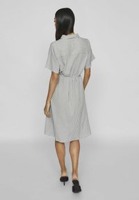Pruhované šaty z světlé šedé a bílé tkaniny, krátké rukávy, pásek v pase a středně dlouhý střih. Hladká textura, casual styl.