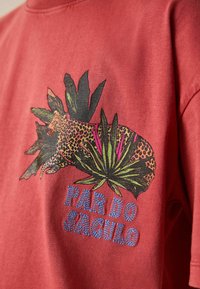 Leopárd trópusi levelekkel díszített grafikával és a "PAR DO SAGULO" felirattal, piros szövet háttéren nyomtatva.
