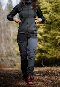 Czarna ocieplana kurtka z wysokim kołnierzem i pikowanym wzorem, zestawiona z czarnymi spodniami cargo na zamek i czerwonymi butami trekkingowymi w naturalnym otoczeniu.