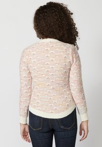 Pull en tricot avec un motif de vagues dans des couleurs pastel sur un fond clair, avec un col et des poignets côtelés blancs.