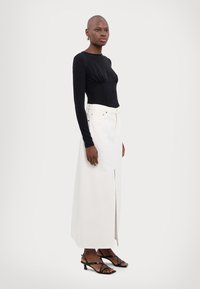 Zwarte lange mouwen top met gerimpelde details, gecombineerd met een witte hoog geprijsde maxi rok met een split aan de voorkant en een ontwerp met vijf zakken.
