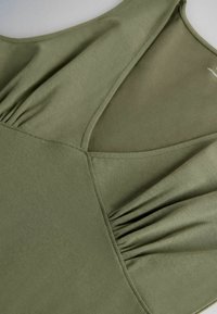 Gros plan sur un tissu vert olive avec un col en V et des détails de couture froncée près des épaules.