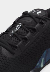 Κοντινή λήψη μαύρου αθλητικού παπουτσιού με ανώτερο μέρος από διχτυωτό υλικό, μαύρα κορδόνια και λεπτομέρεια σόλας με μπλε σχέδιο, με ετικέτα "CX12" στη γλώσσα.